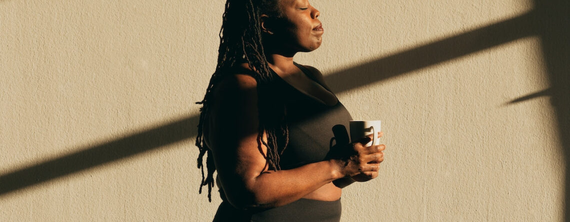 A Black woman wearing athletic attire and holding a mug while closing her eyes | How Plant Medicine and Breath Work Compliment One Another | Sugar Magnolia