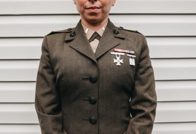 Close-up of a military veteran wearing a decorated uniform with medals and service ribbons, standing in front of a light wall.