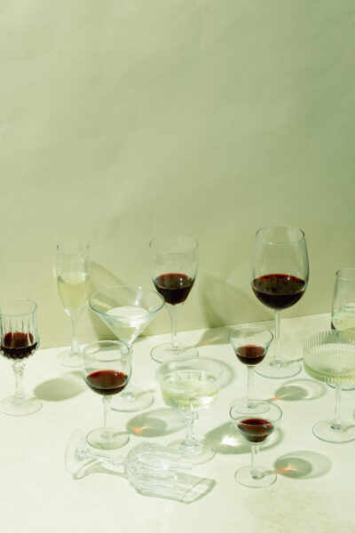 Assorted wine glasses filled with red and white beverages on a white surface with shadows