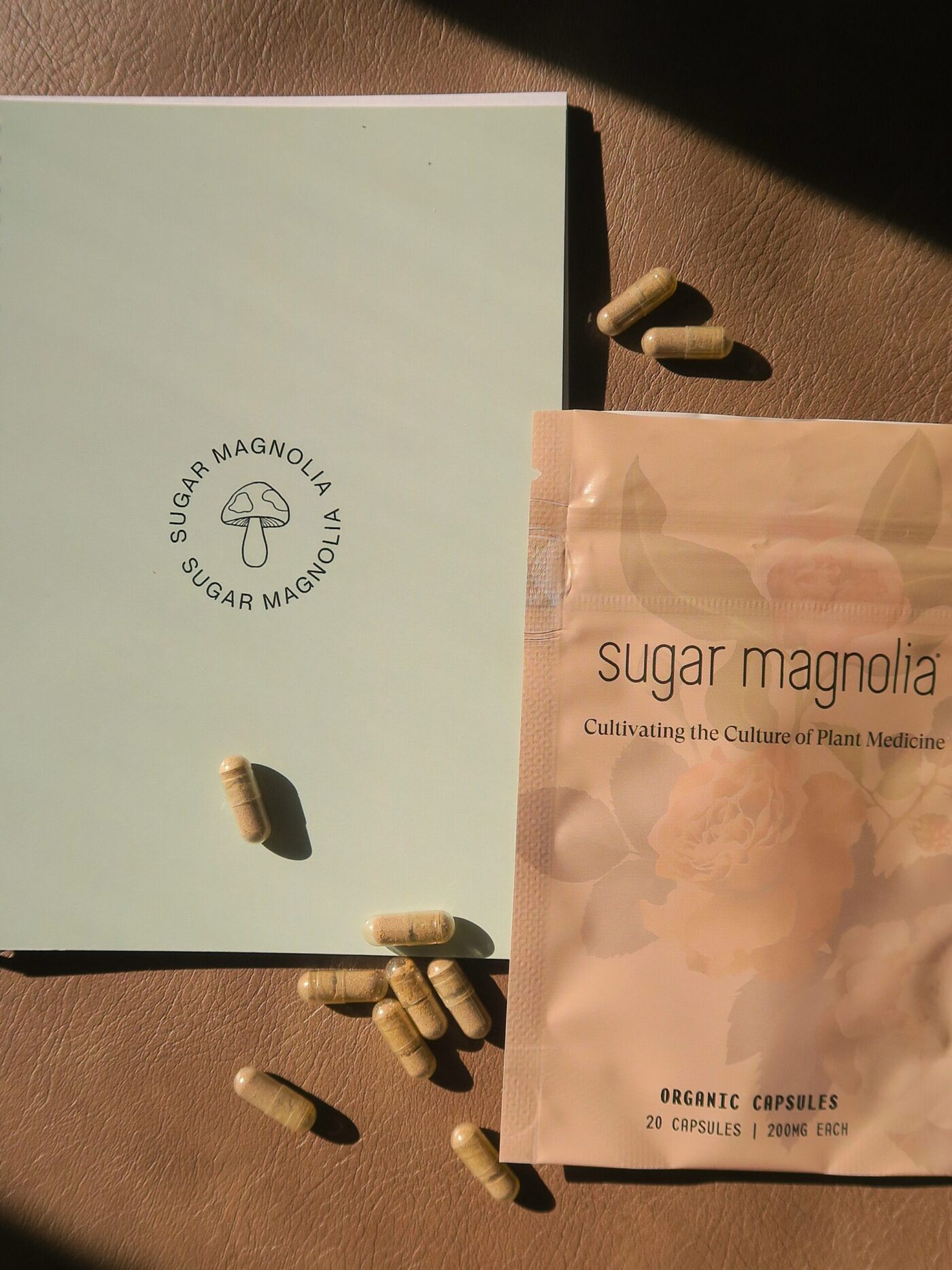 Sugar Magnolia journal and organic capsules pouch with scattered capsules on a leather surface.