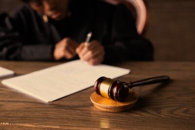 Judge’s wooden gavel on a desk with blurred person signing legal documents in the background.