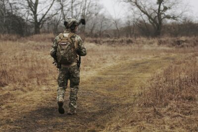 US military veteran walking through a quiet field in full combat gear on a cloudy day.