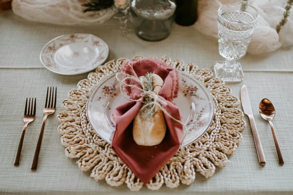 Rustic holiday table setting with vintage plates, a burgundy napkin, and artisan bread decorated with herbs.