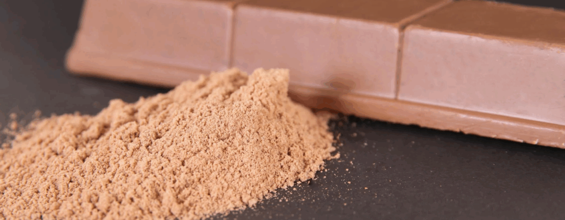 Cocoa powder and milk chocolate bar on a dark background