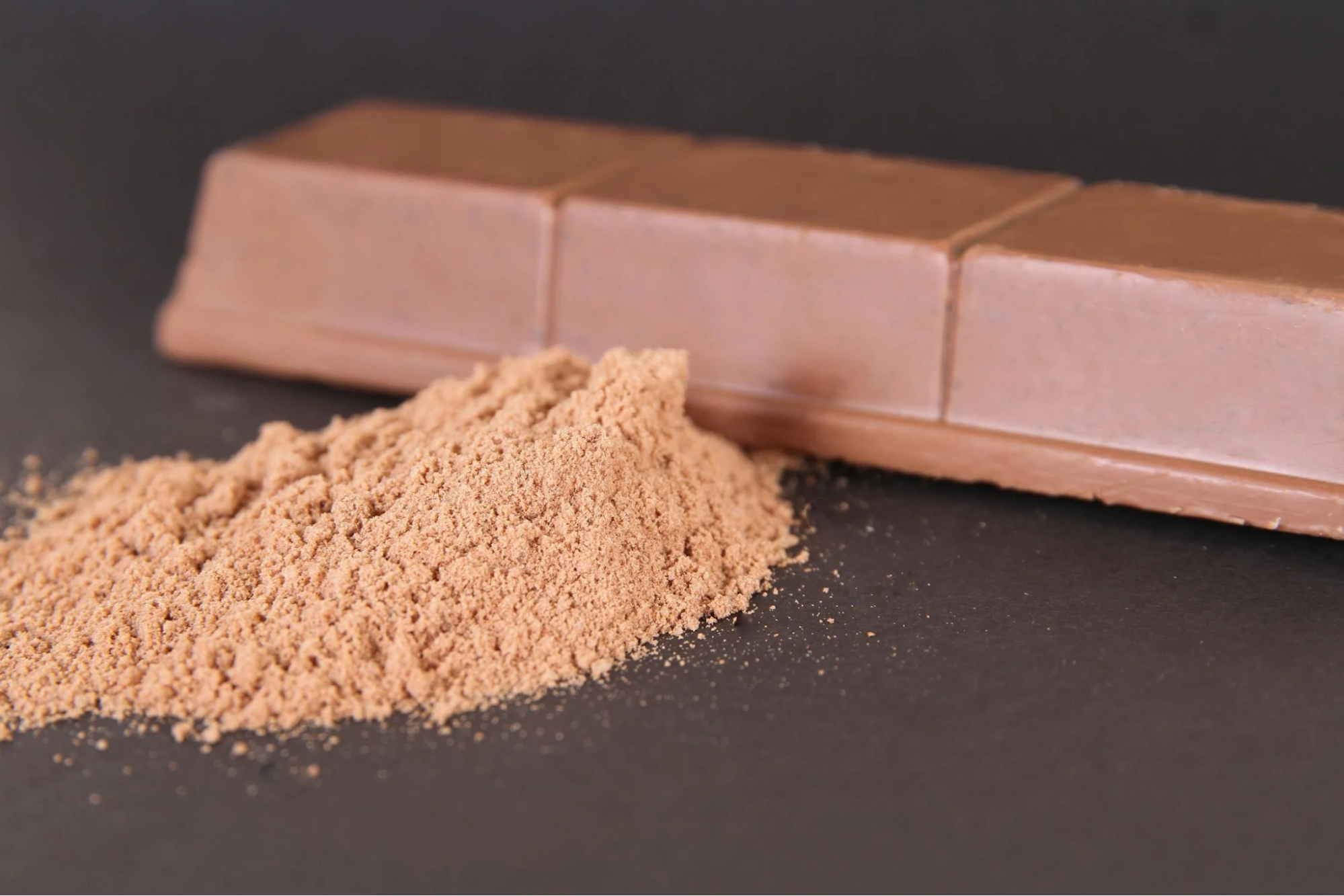 Cocoa powder and milk chocolate bar on a dark background