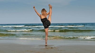 Woman stretching with high leg lift on the beach, facing the ocean